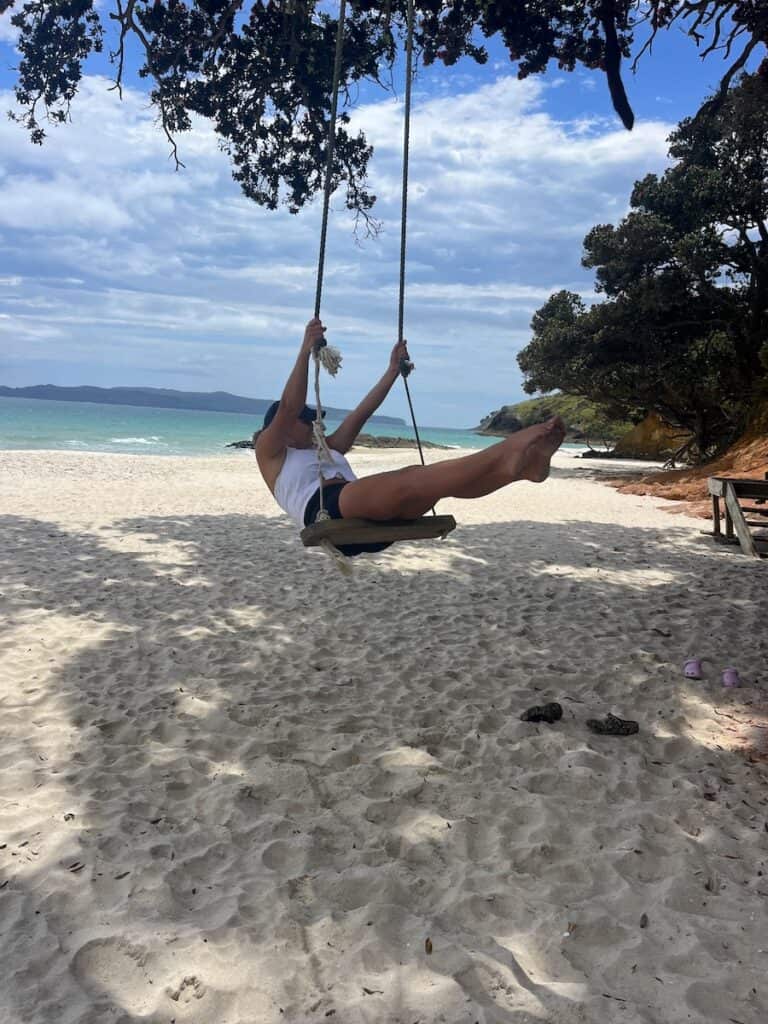 A girl swinging over the sand on the Otama Beach swing