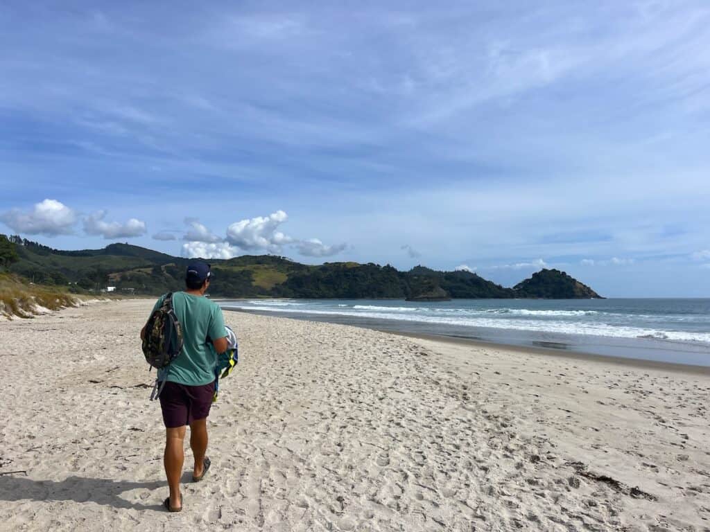 Man walking along the white sand at Whangapoua Beach