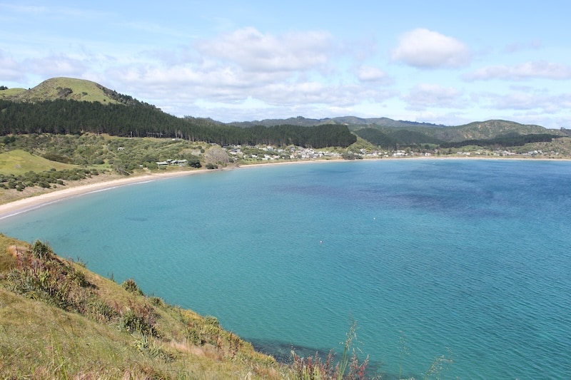 The blue water of Opito Bay with rolling hills in the background