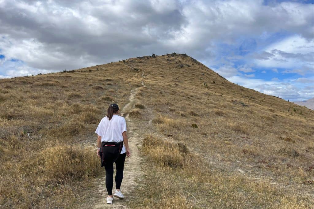 Girl walking up a grassy hill to a lookout in Queenstown