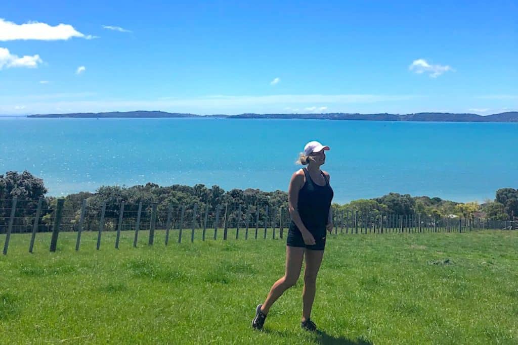 Girl walking in a grass paddock with the ocean in the background