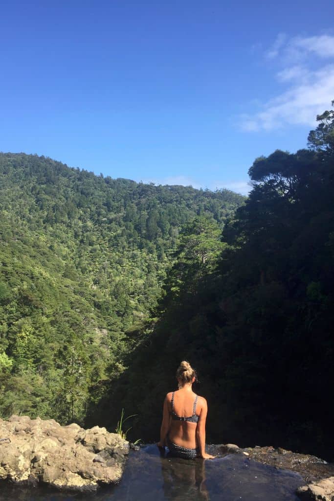 Girl sitting at the top of Kitekite Falls and looking out to the bush in the distance