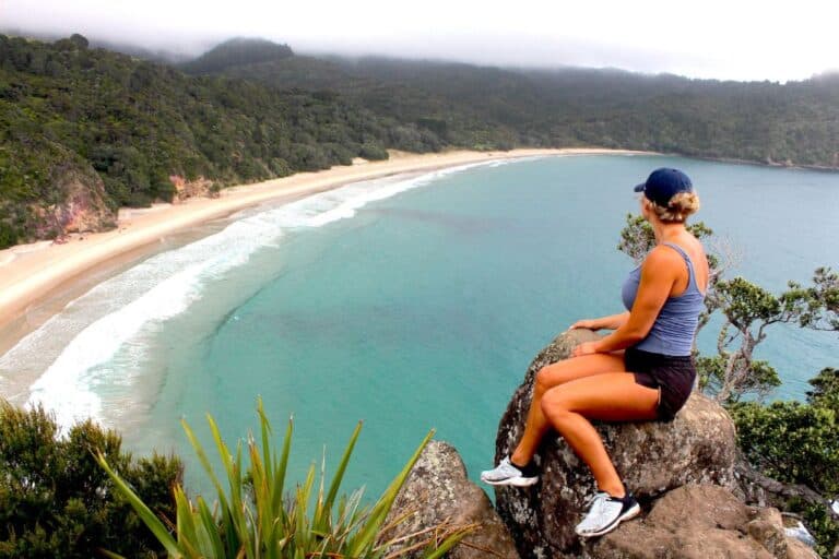 A girl sitting on a rock at a lookout looking over the bright blue ocean.