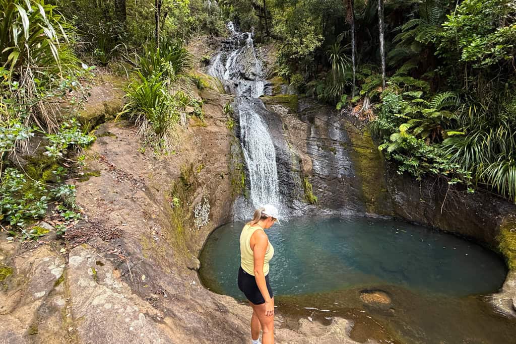 Woman standing in front of Fairy Falls with water flowing behind.