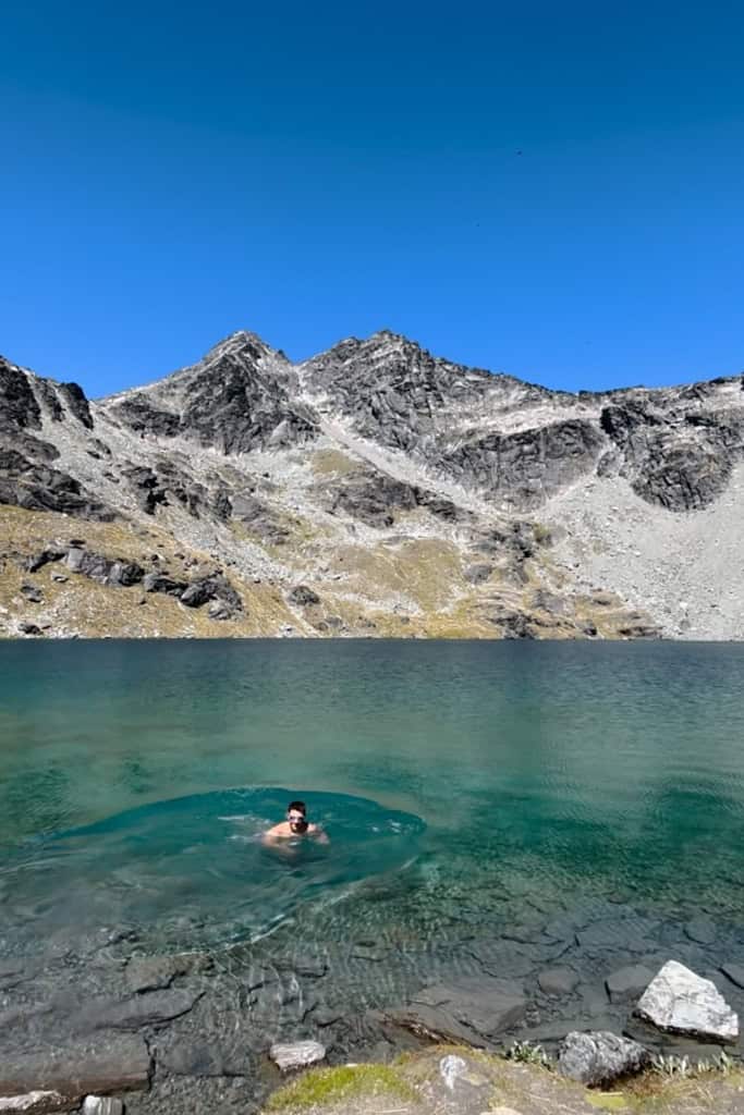 Man swimming in the colourful blue water on the Lake Alta hike.