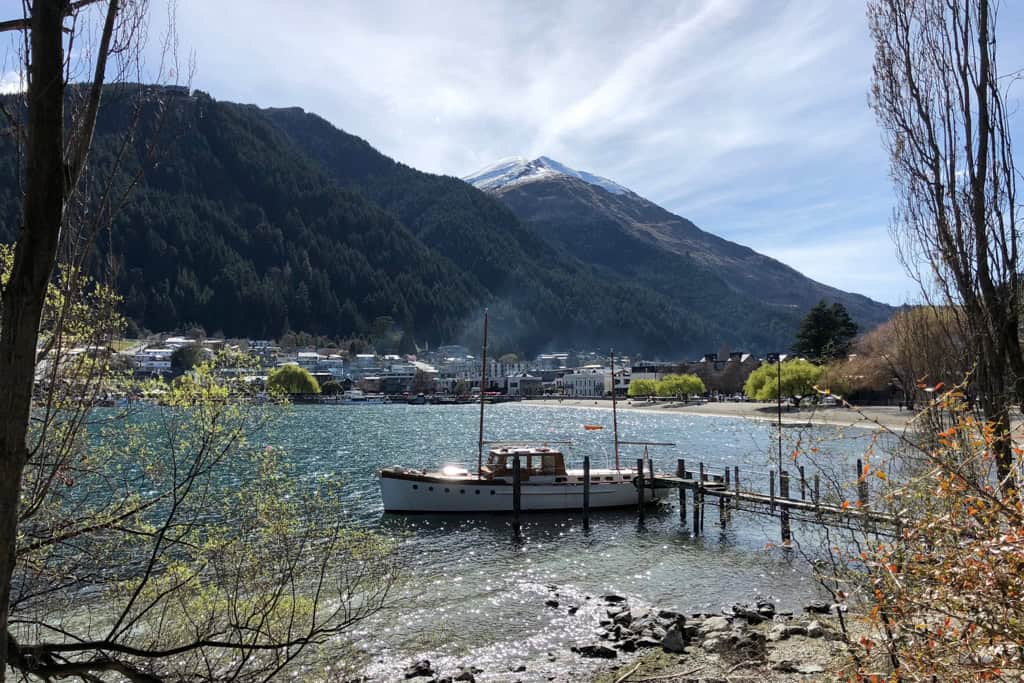 A sailing boat on the waters edge with Queenstown in the background.