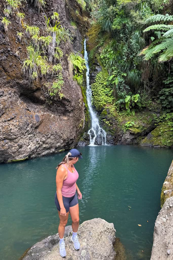 Woman standing on a rock looking back at the water flowing into the pool at the bottom of the falls.