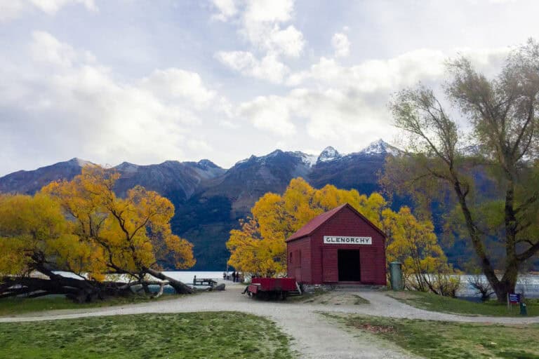 The Red Boat shed on the lakes edge surrounded by mountains and autumn trees.