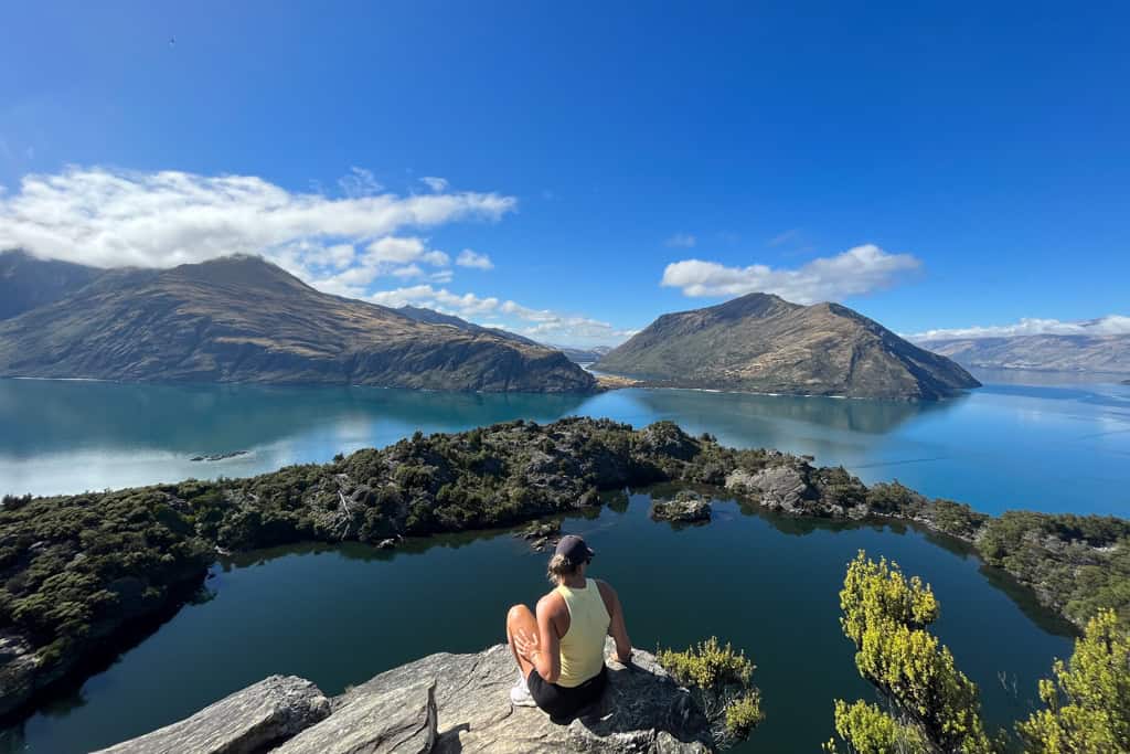 Woman sitting on a rock looking out over a lake towards the mountains in Wanaka.