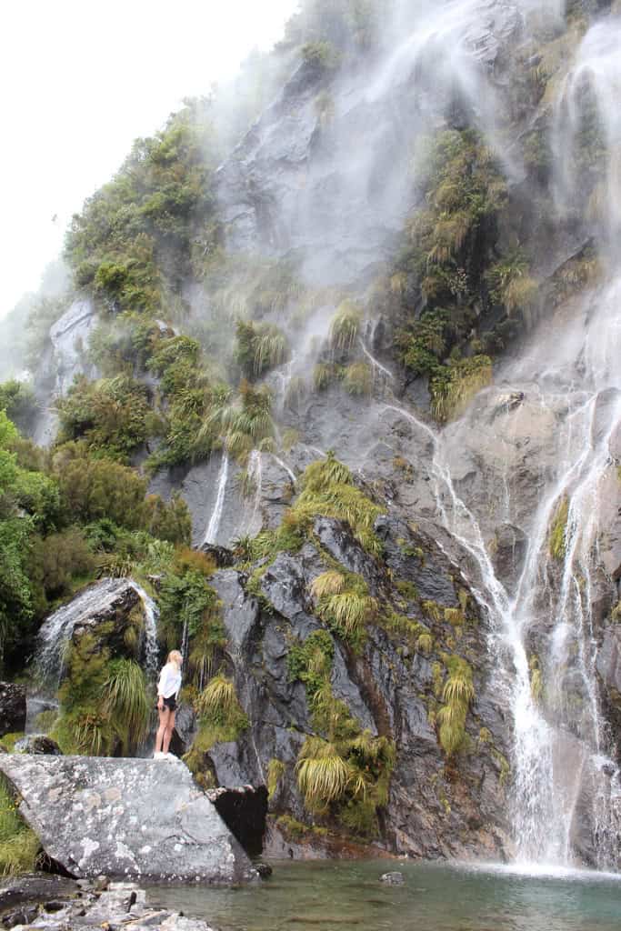 Woman standing at the base of Wishbone falls looking up as water falls down around her.