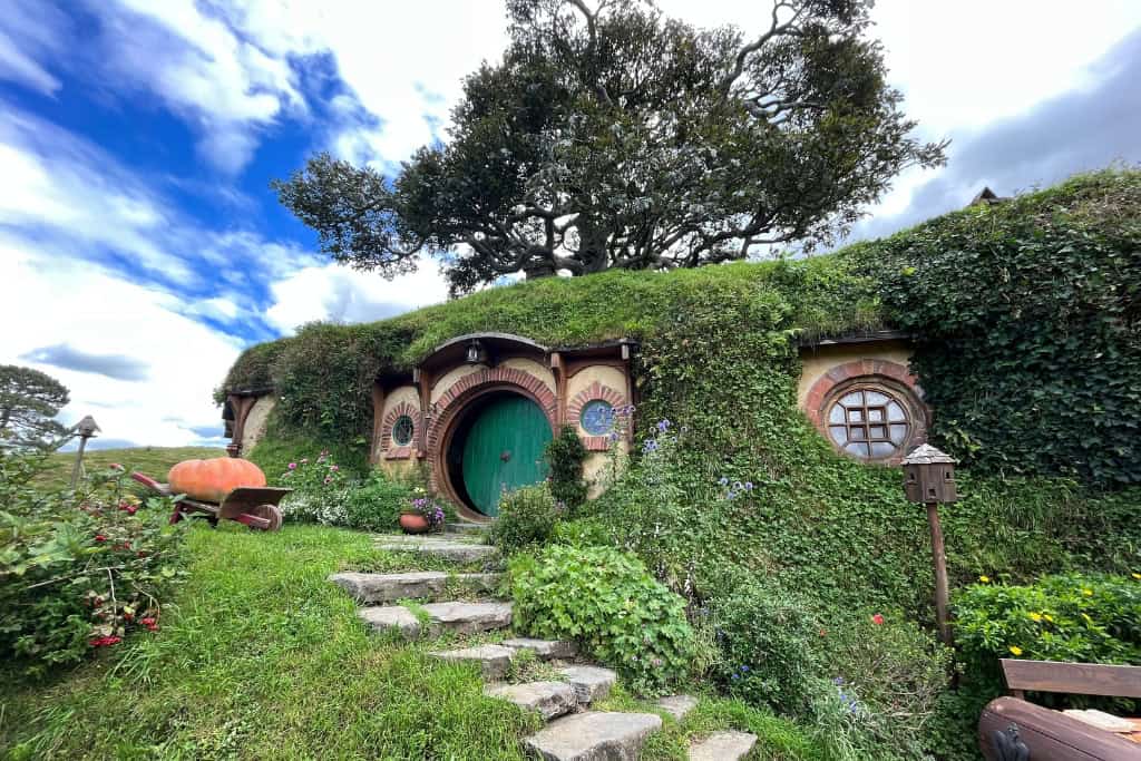 A small hobbit house built in to the hill surrounded by gardens and trees.
