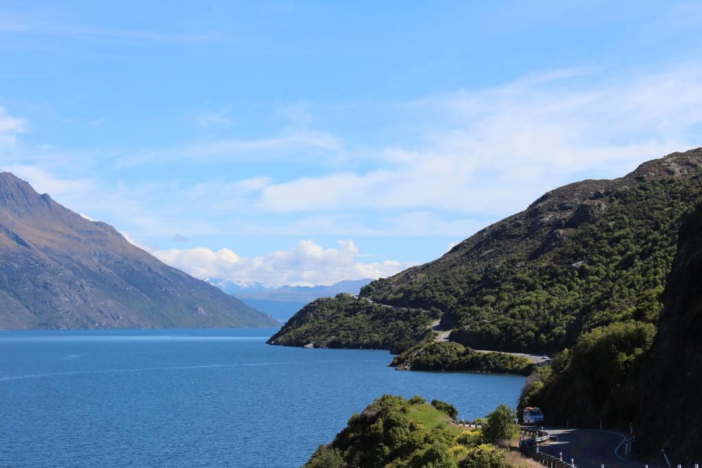 The road winding along the edge of the lake surrounded by mountains in Queenstown.