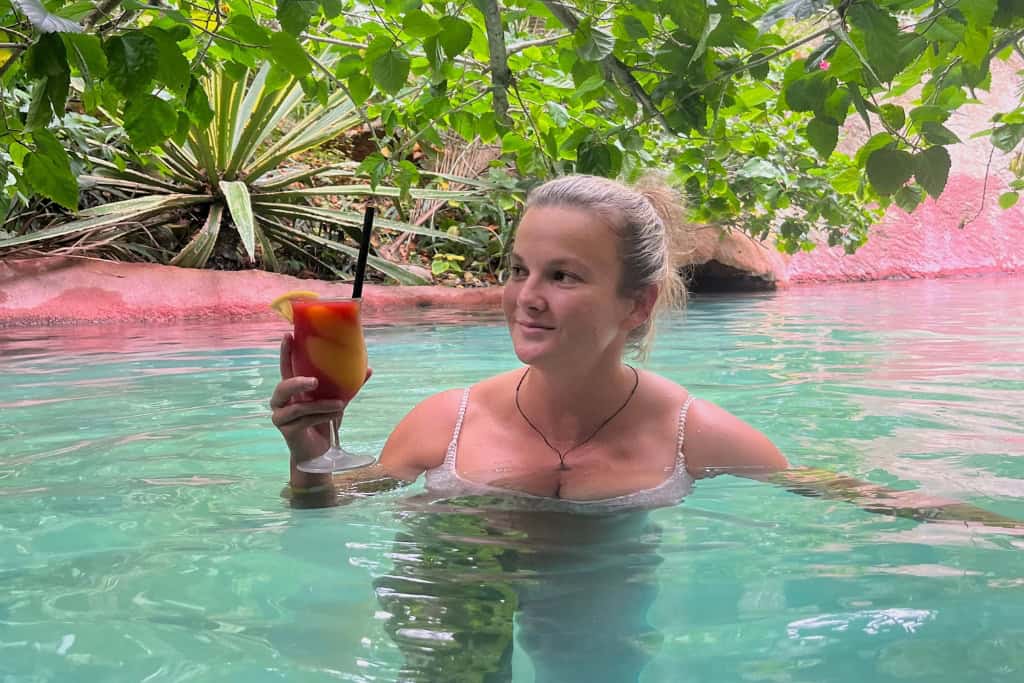 Woman holding a colourful cocktail while relaxing in the hot pools.