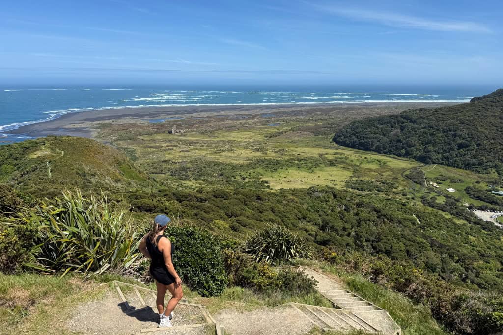 Woman standing on top of a hill and looking out at the view on the Omanawanui Track, one of Auckland's best walks.