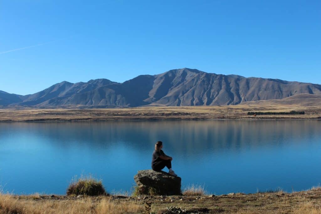 Woman sitting on a rock looking out at the view of the lake on the Mt John Summit Track