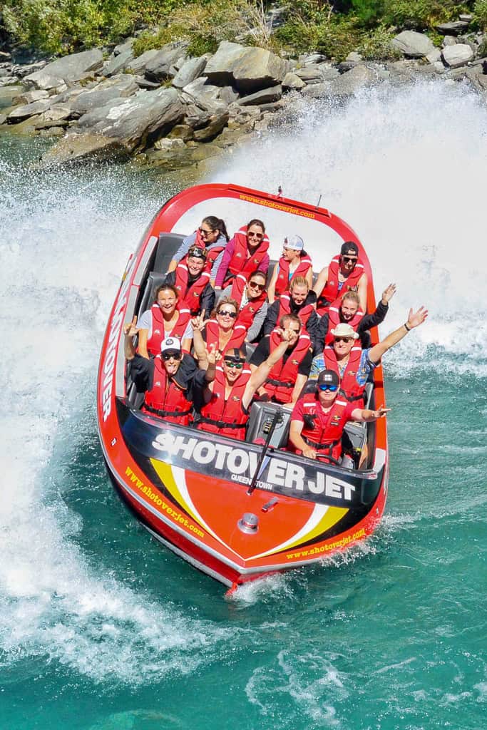 People in a jet boat with their arms up as the boat does a spin in the water.