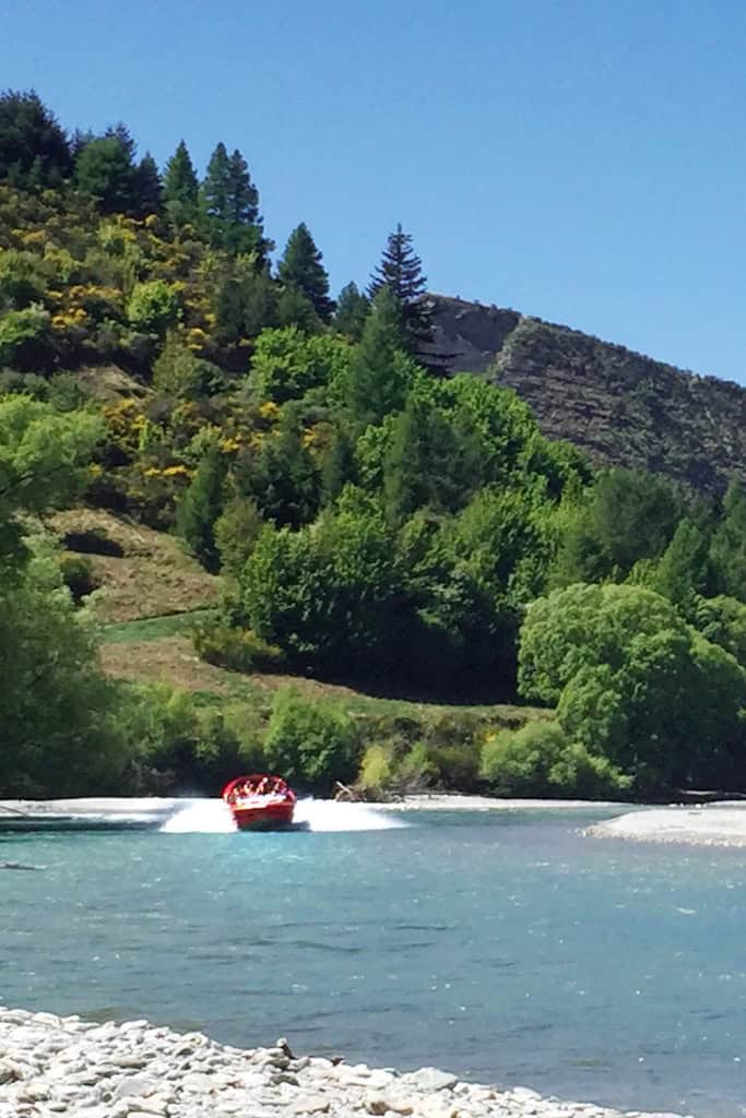 A jet boat driving down the river on a sunny day in Queenstown.