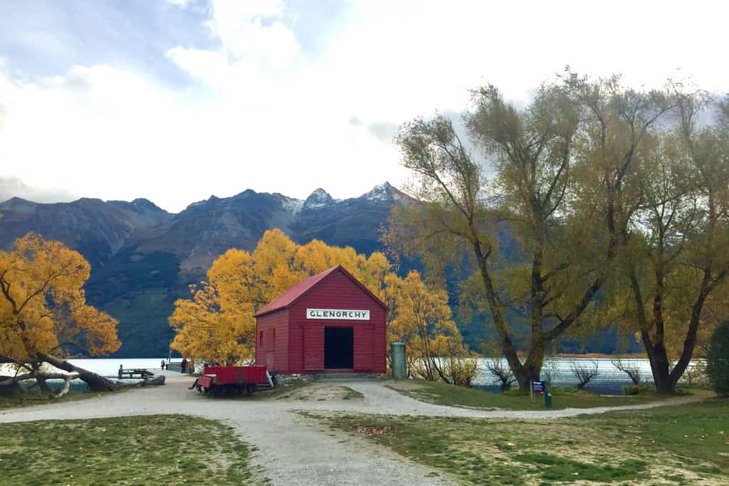 The red shed in Glenorchy surrounded by snowy mountains and autumn trees.