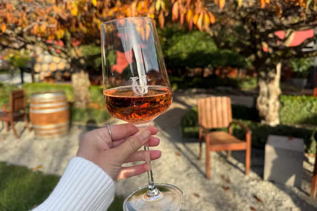 A hand holding a glass of wine in the garden at the winery.