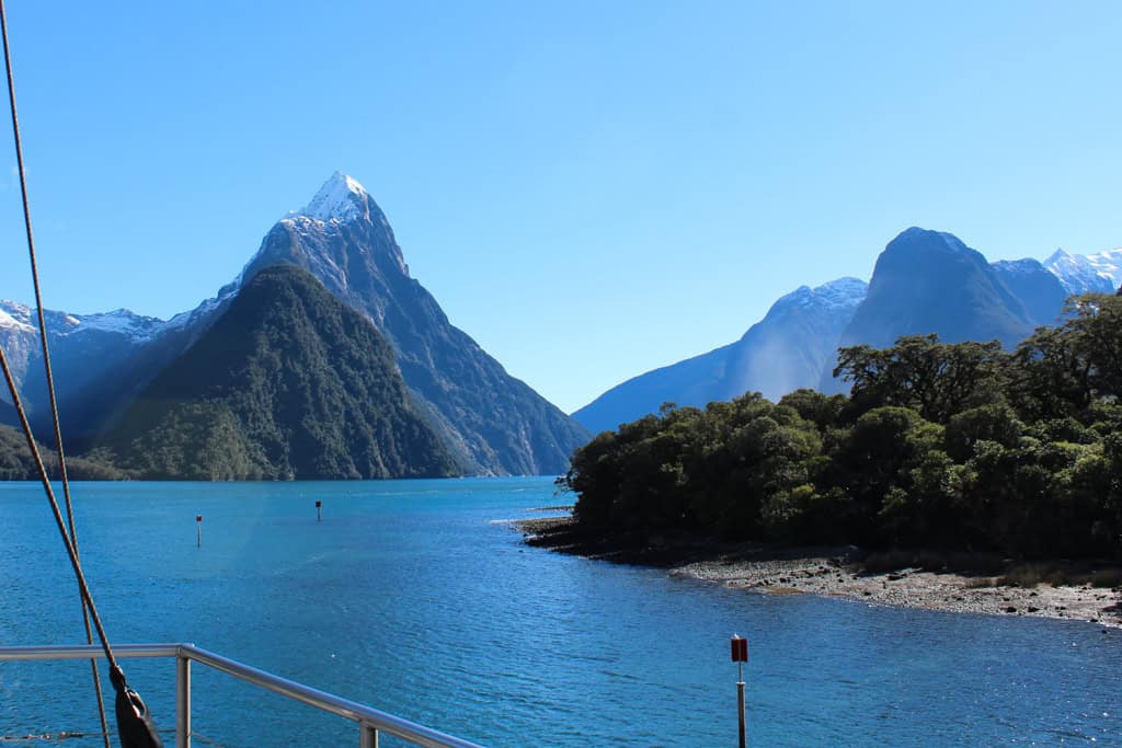 The tall mountain peaks in Milford Sound from a boat on a sunny day.