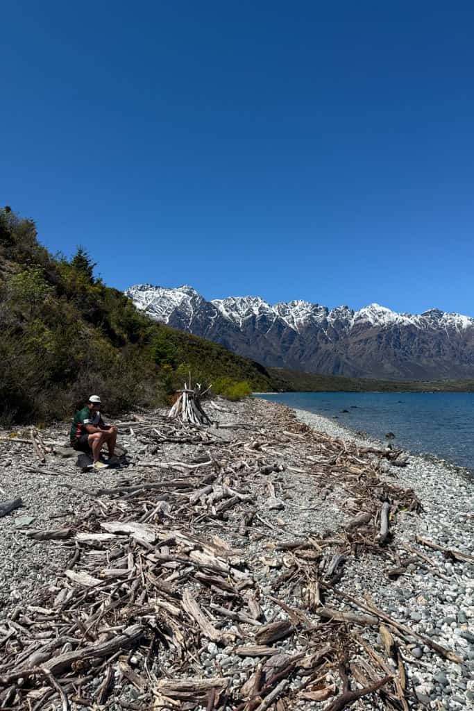 A person sitting on the beach down one of the side tracks on the Jacks point trail.
