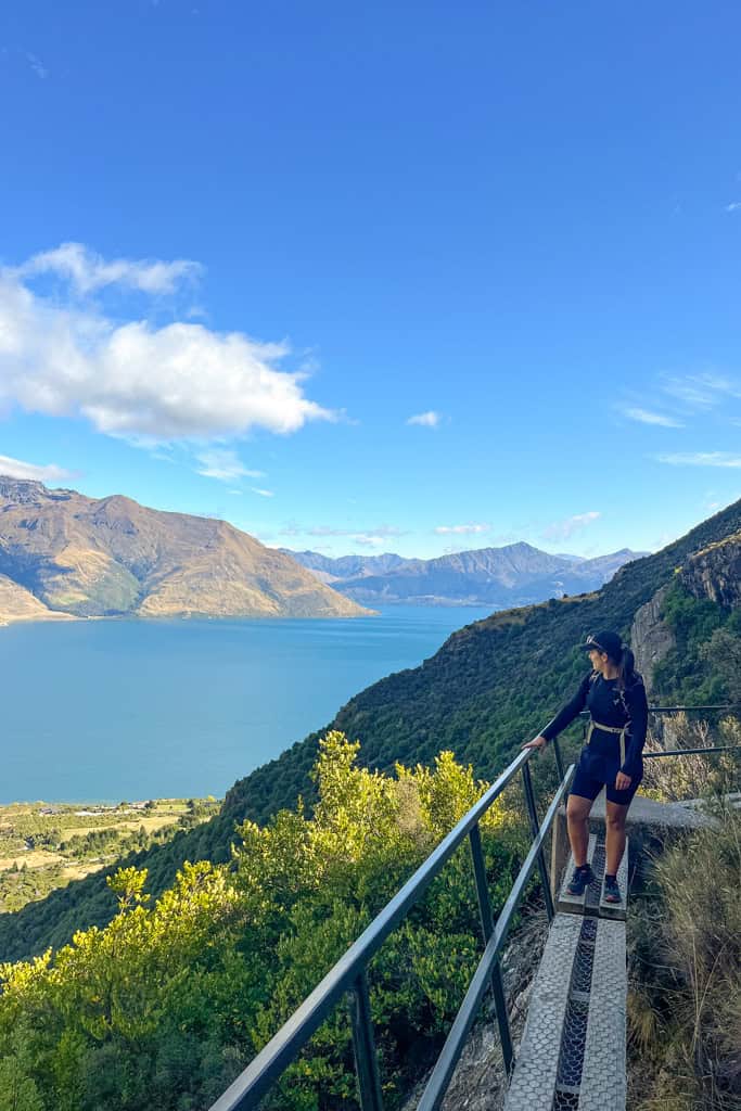 Person standing on the narrow walkway looking out to the lake and mountains.