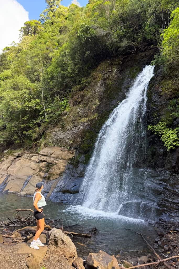 Woman standing enjoying the waterfall along the Upper Nihotupu Falls walk in Auckland.