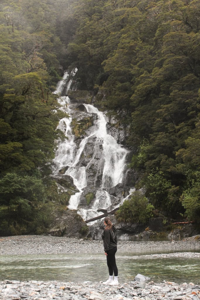 Person standing and looking at Fantail Falls from across the river.