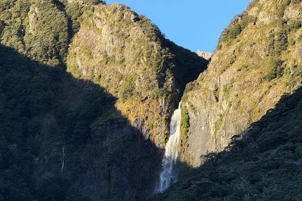 The sun sets behind the hills bringing a shadow over The Devils Punchbowl Waterfall in Arthurs pass on the South Island of New Zealand.