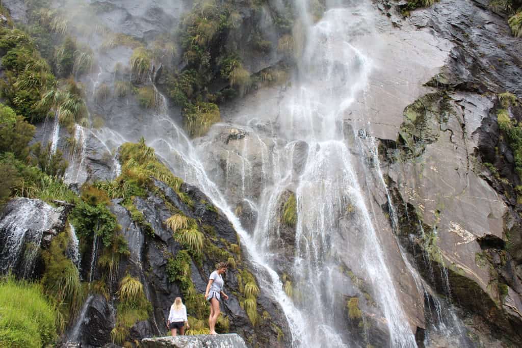Two people standing at the base of Wishbone Falls waterfall in New Zealand's South Island.